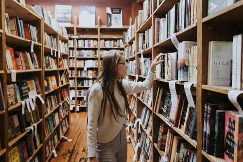 Момиче, което избира книга от рафтовете на изпълнена с книги библиотека.