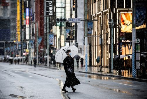 Мъж с маска и чадър се разхожда по улиците на Токио по време на пандемията
