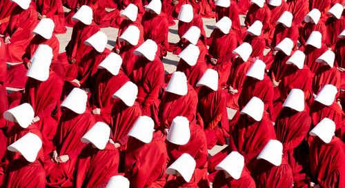 Жени в червени наметала и бели шапки, които скриват лицата им