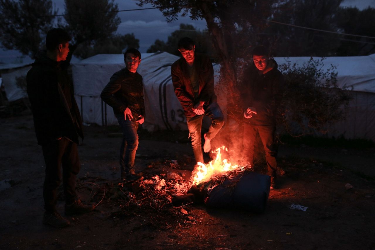 Хора се топлят край огъня в лагера „Мория“