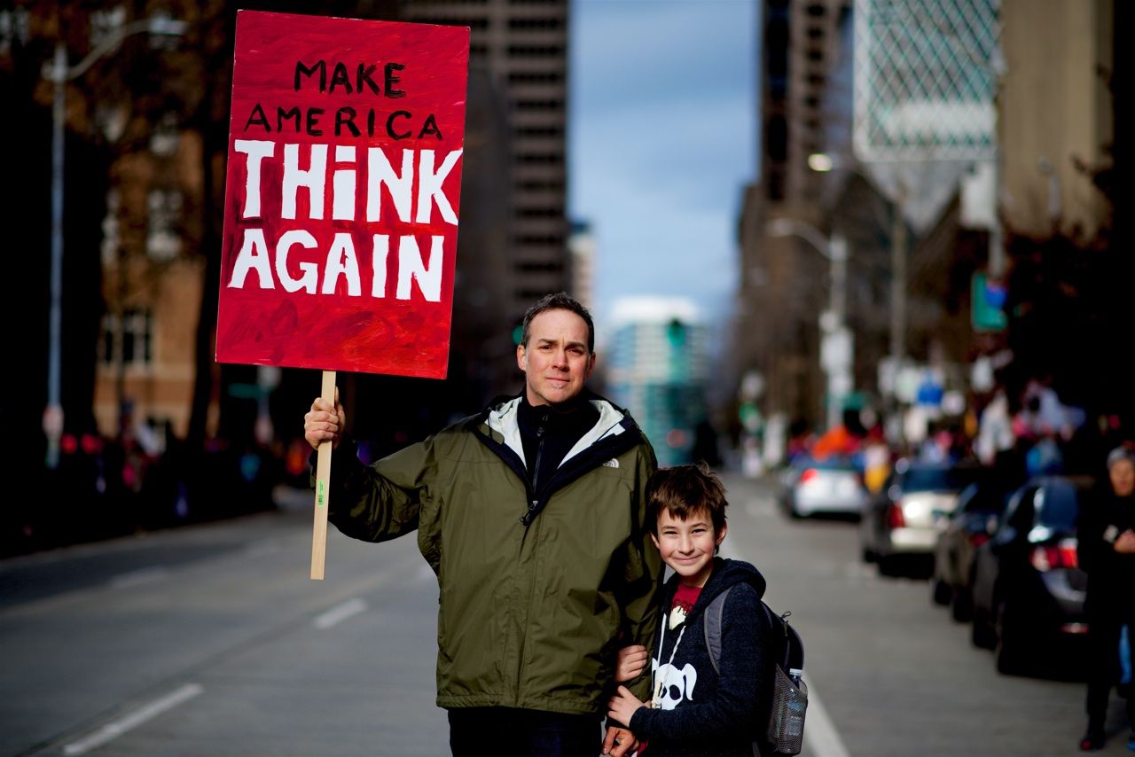 Мъж и дете, мъжът държи табела с надпис „Накарайте Америка да мисли отново“